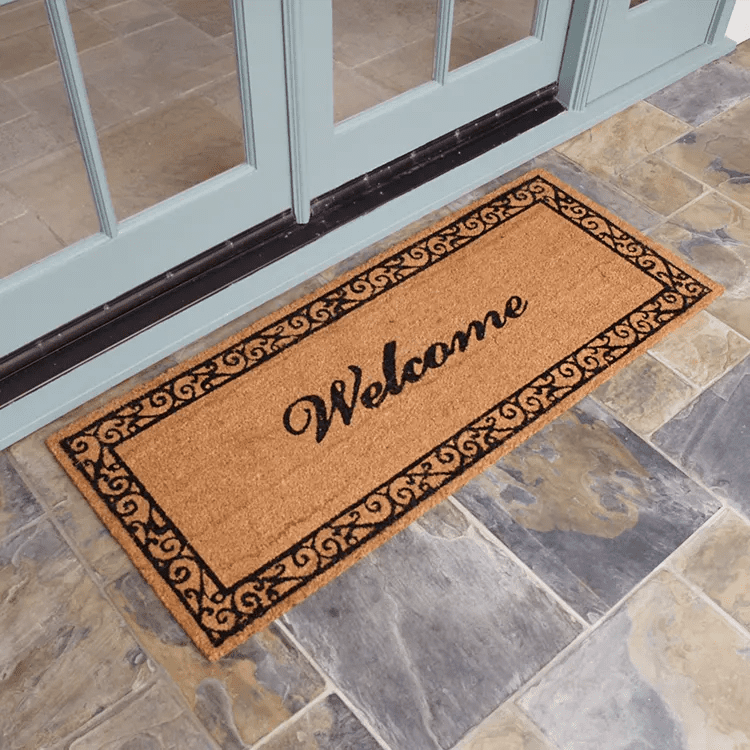 Side View of Doormat with "Welcome" Written in Cursive, and a Swirl Border design in Front of White Double Doors