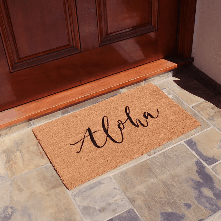 Front Side View of a Doormat with "Aloha" Written in Cursive in Front of a Brown Front Door