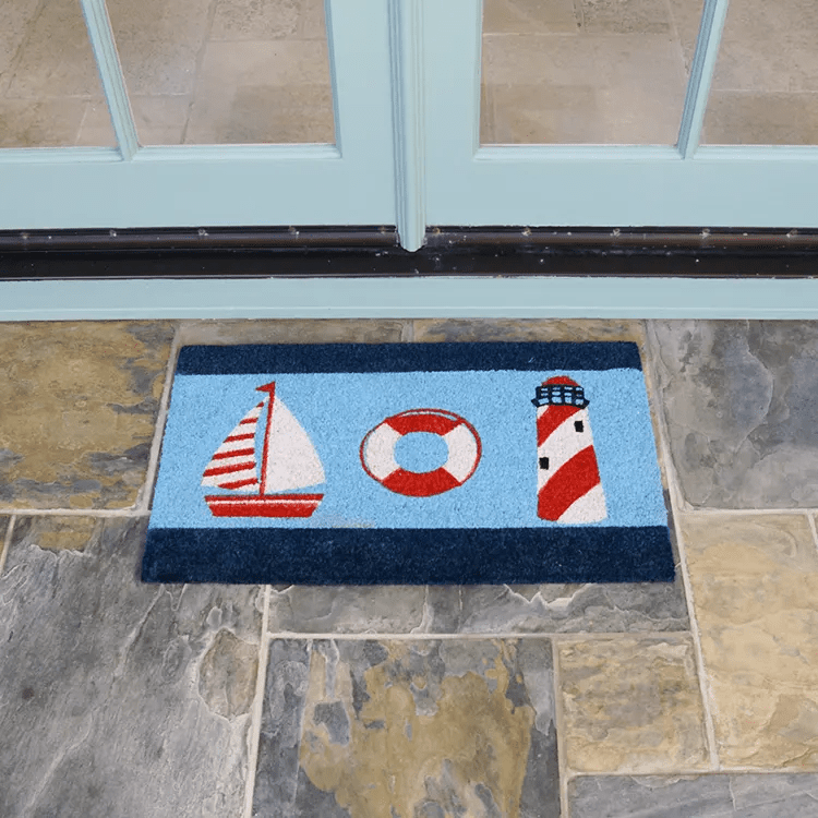 Light Blue Doormat with a Cartoon Sailboard, Life Buoy, and Light House Design in Front of White Double Doors