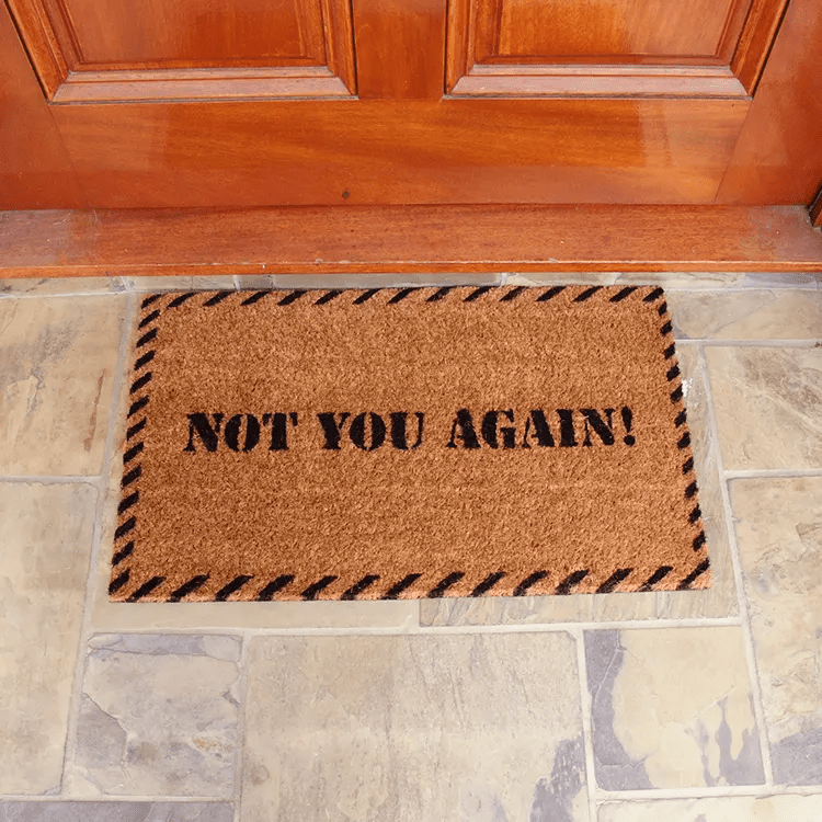 Doormat with "Not You Again!" Text is in Front of Wood Door