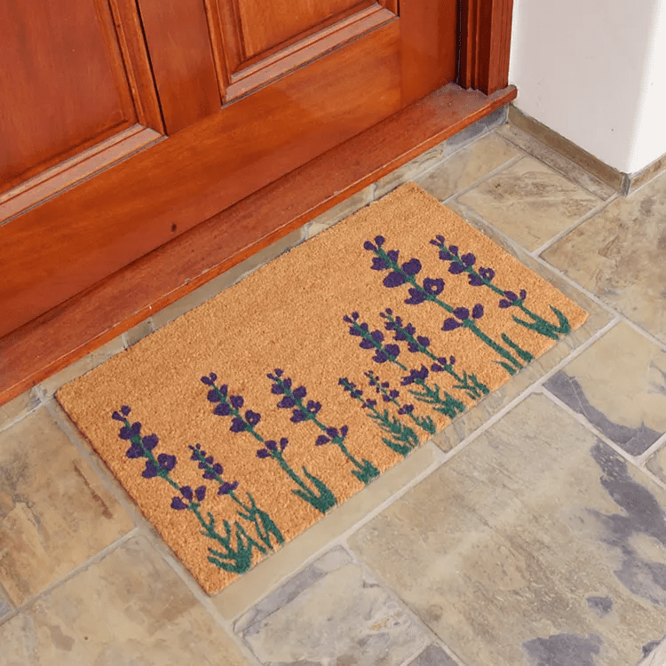 Side View of a Welcome Mat with 3 Red Daisies and Welcome Text in Front of a Brown Door