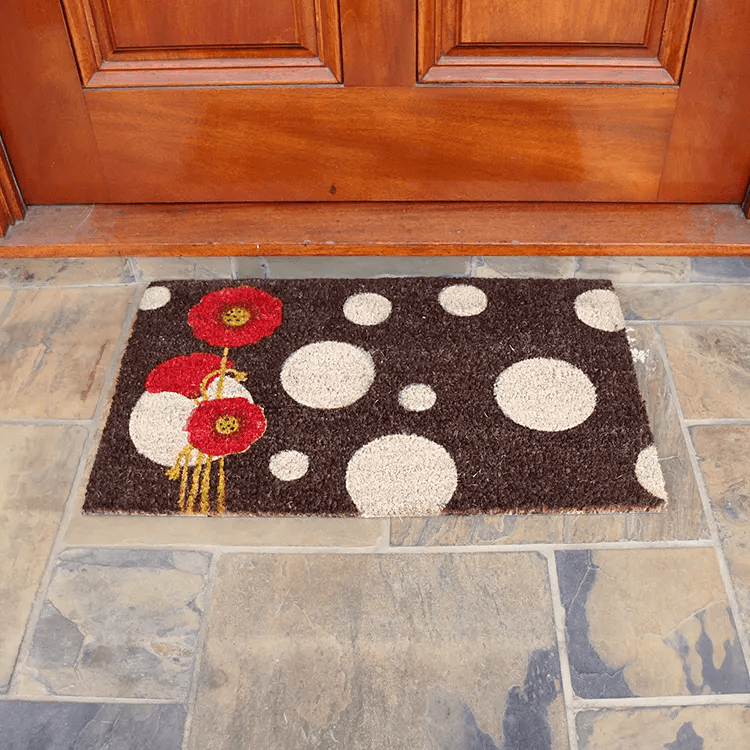 Front View of a Black Doormat with Red Poppies and White Polkadots in Front of a Brown Door